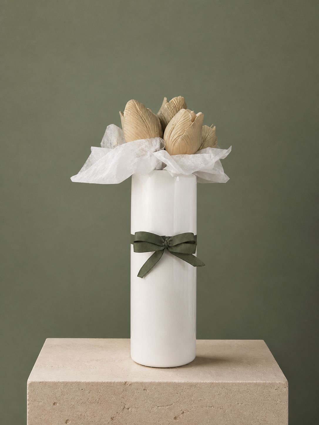 Tall taupe tulip candles arranged in a white vase with an olive ribbon