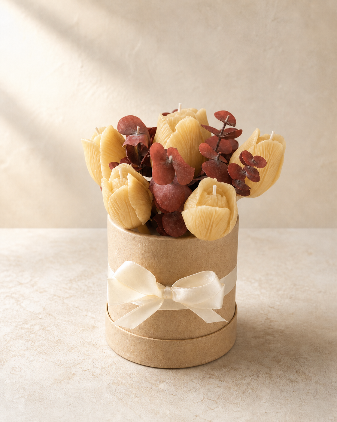 Warm amber tulip candles with rust-toned eucalyptus in an ivory hatbox