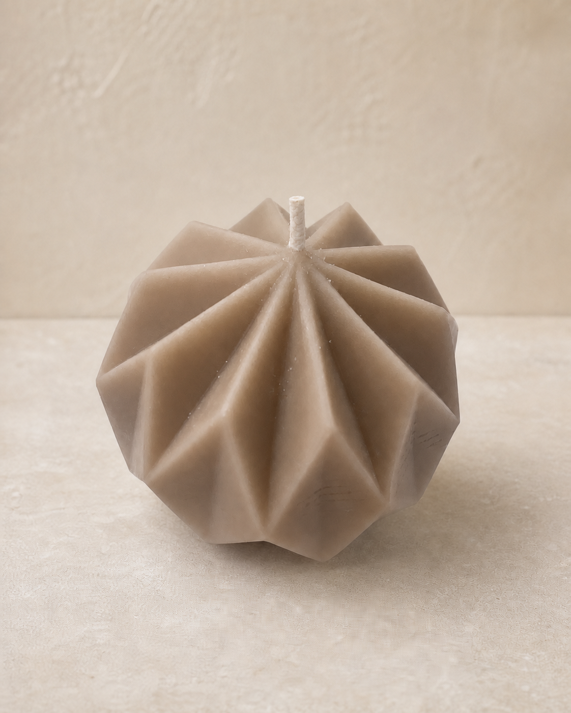Taupe round sculptural candle with folded geometric pleats
